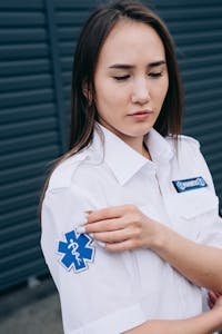 Female paramedic adjusts her medical badge outdoors, portraying professionalism.